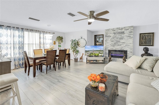 living area with a textured ceiling, ceiling fan, a fireplace, and visible vents