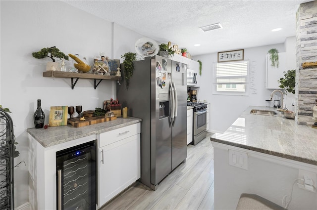 kitchen with stainless steel appliances, white cabinetry, a sink, a textured ceiling, and beverage cooler