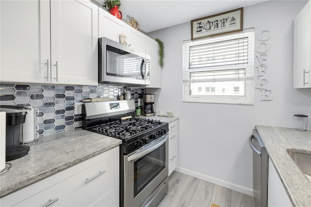 kitchen with white cabinetry, baseboards, light wood-style floors, appliances with stainless steel finishes, and decorative backsplash