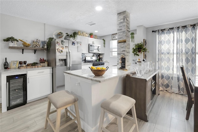 kitchen featuring appliances with stainless steel finishes, wine cooler, a breakfast bar area, and white cabinets