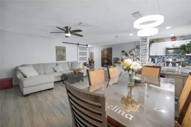 dining area with light wood-type flooring, a barn door, visible vents, and ceiling fan