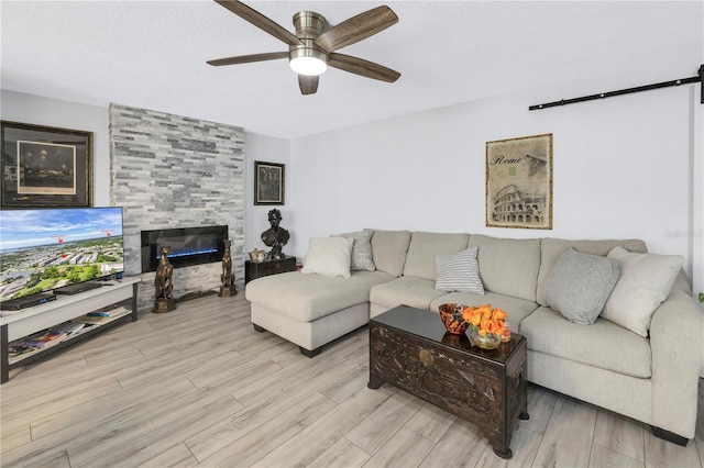 living area with light wood-style flooring, a fireplace, a ceiling fan, and a textured ceiling