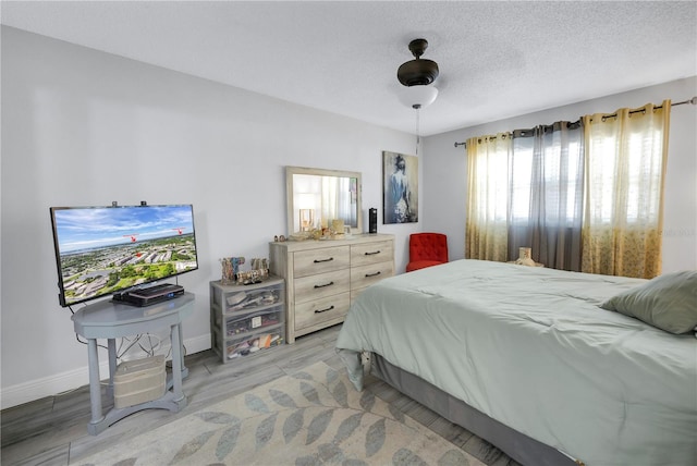 bedroom with light wood-type flooring, a textured ceiling, and baseboards