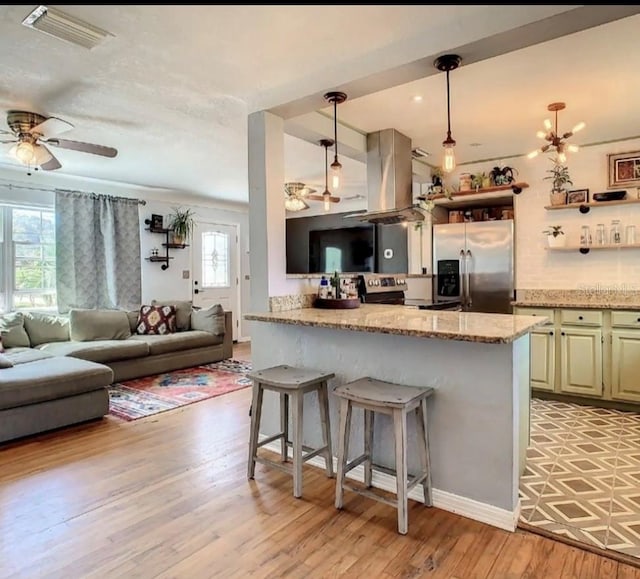 kitchen featuring stainless steel fridge, island exhaust hood, hanging light fixtures, light hardwood / wood-style flooring, and a kitchen bar