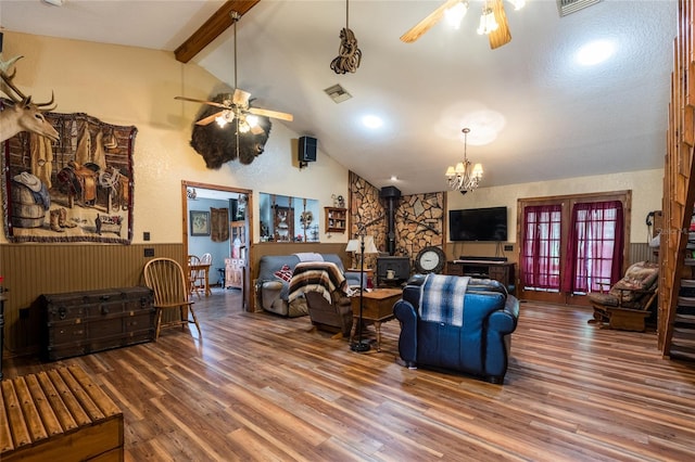 living room featuring french doors, beamed ceiling, ceiling fan with notable chandelier, dark wood-type flooring, and a wood stove