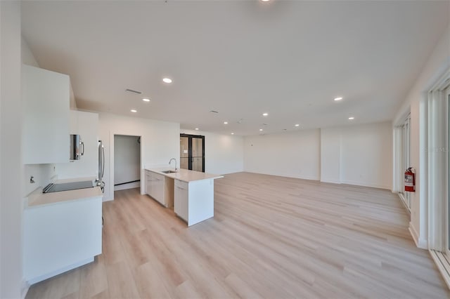 kitchen with light countertops, appliances with stainless steel finishes, white cabinetry, a sink, and light wood-type flooring