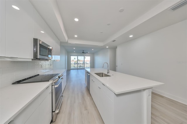 kitchen featuring a sink, appliances with stainless steel finishes, light wood finished floors, modern cabinets, and a raised ceiling