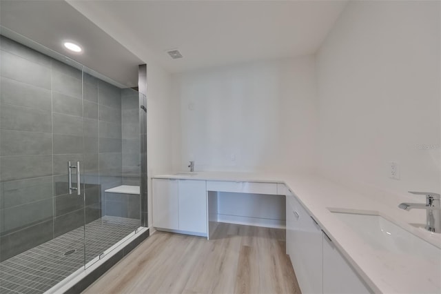 full bath featuring double vanity, a shower stall, a sink, and wood finished floors