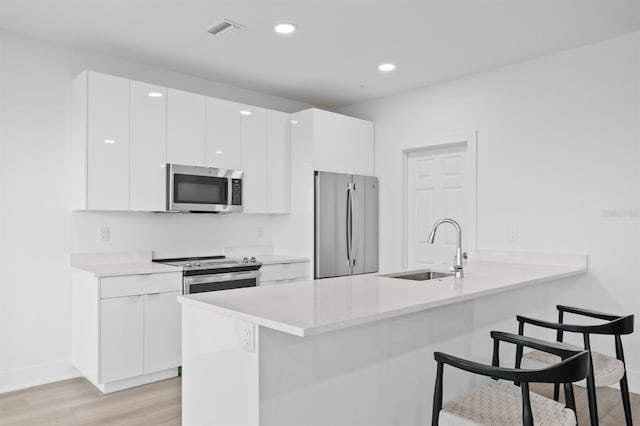 kitchen with a sink, a kitchen breakfast bar, modern cabinets, stainless steel appliances, and visible vents
