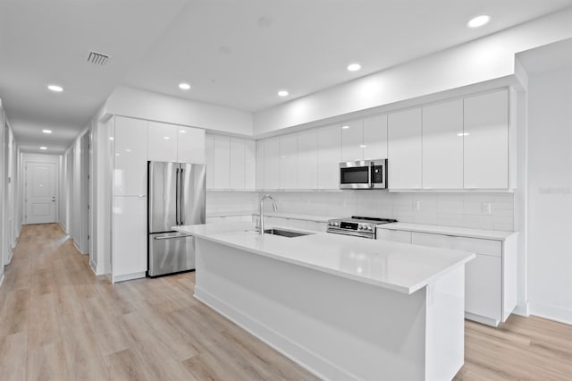 kitchen with white cabinetry, light wood-type flooring, stainless steel appliances, a sink, and modern cabinets