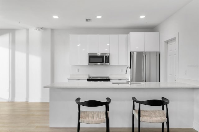 kitchen featuring white cabinetry, a sink, stainless steel appliances, and a kitchen breakfast bar