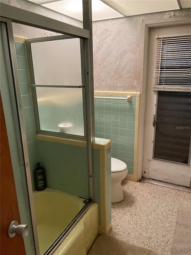 bathroom featuring toilet, enclosed tub / shower combo, and tile walls