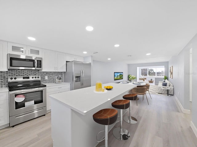 kitchen featuring a kitchen island, white cabinets, a breakfast bar, stainless steel appliances, and light wood-type flooring