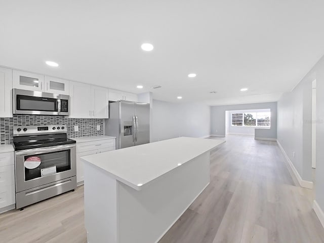 kitchen with stainless steel appliances, a kitchen island, tasteful backsplash, white cabinets, and light wood-type flooring