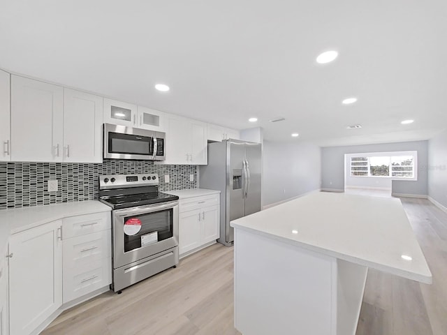 kitchen with a kitchen island, white cabinets, light hardwood / wood-style flooring, backsplash, and stainless steel appliances