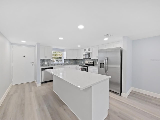 kitchen featuring light wood-type flooring, stainless steel appliances, white cabinets, a kitchen island, and tasteful backsplash