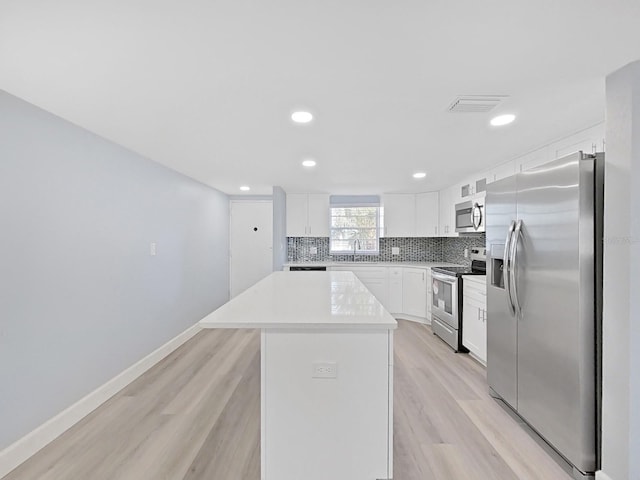 kitchen with a kitchen island, tasteful backsplash, light hardwood / wood-style flooring, appliances with stainless steel finishes, and white cabinetry