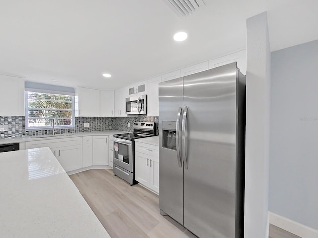 kitchen with sink, backsplash, light hardwood / wood-style floors, stainless steel appliances, and white cabinetry