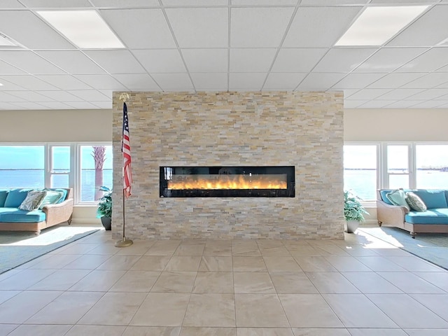 unfurnished living room with a fireplace, a drop ceiling, and light tile floors