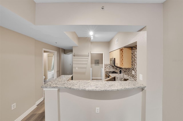 kitchen featuring sink, stainless steel appliances, tasteful backsplash, light stone counters, and kitchen peninsula