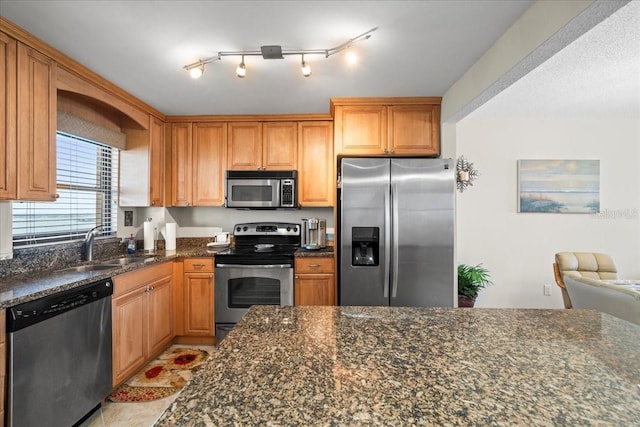 kitchen with sink, light tile floors, rail lighting, dark stone countertops, and stainless steel appliances