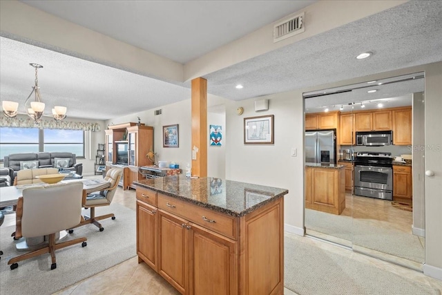 kitchen featuring light tile floors, dark stone counters, appliances with stainless steel finishes, a chandelier, and decorative light fixtures