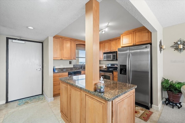 kitchen featuring appliances with stainless steel finishes, dark stone countertops, light tile flooring, a textured ceiling, and a center island