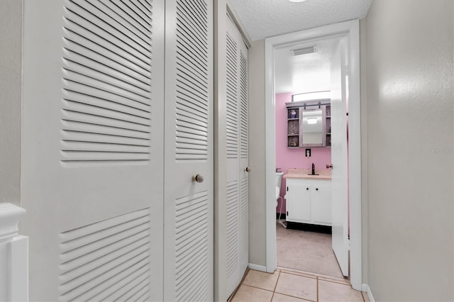 hallway with a textured ceiling, sink, and light tile floors