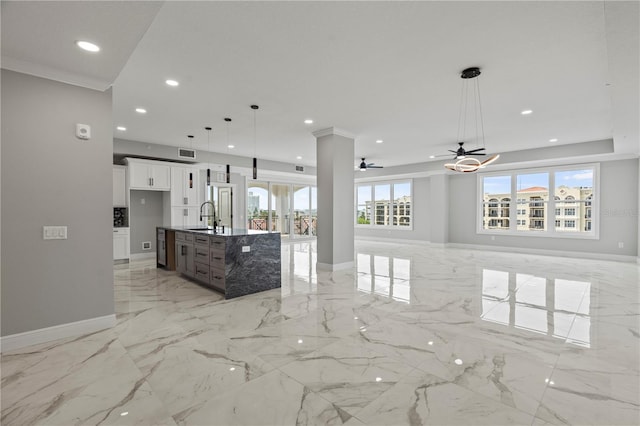 kitchen with decorative light fixtures, ornamental molding, light tile floors, ceiling fan, and an island with sink