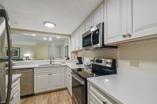 kitchen featuring stainless steel appliances, a textured ceiling, white cabinets, light wood-type flooring, and sink