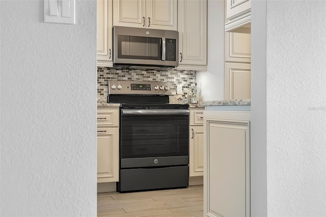 kitchen with backsplash, appliances with stainless steel finishes, light hardwood / wood-style flooring, light stone counters, and cream cabinetry