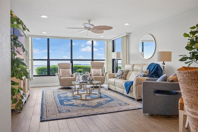 living room featuring a wall of windows, ceiling fan, and light wood-type flooring