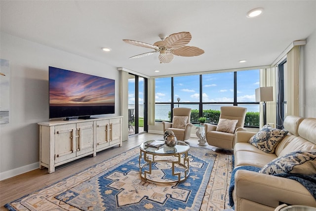 living room featuring expansive windows, light hardwood / wood-style floors, ceiling fan, and a water view