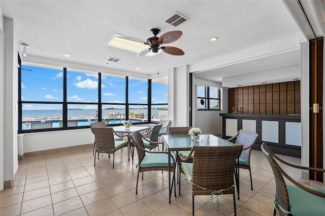 dining space with a water view, a textured ceiling, ceiling fan, and light tile floors