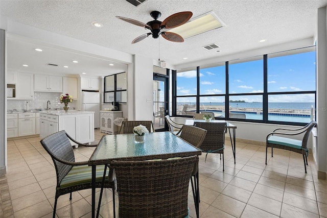 tiled dining space featuring a water view, a textured ceiling, and ceiling fan