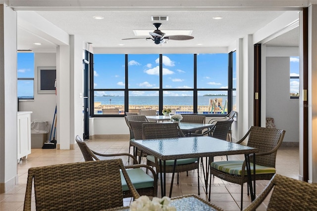 dining room with a water view, a textured ceiling, light tile flooring, and ceiling fan