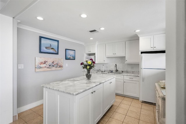 kitchen with white refrigerator, tasteful backsplash, white cabinets, and a center island