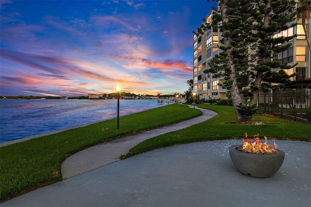 view of property's community with a lawn, a water view, and an outdoor fire pit