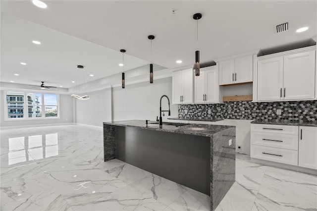 kitchen featuring white cabinetry, a kitchen island with sink, hanging light fixtures, and dark stone counters