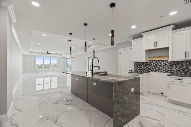 kitchen featuring tasteful backsplash, ceiling fan, pendant lighting, and a center island with sink