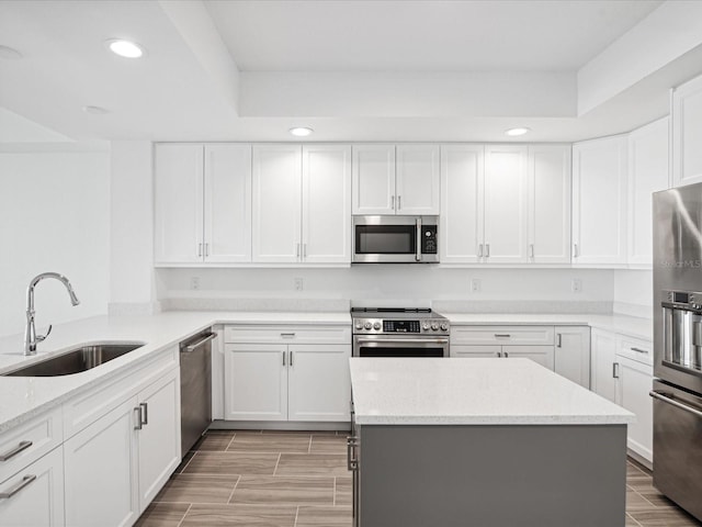 kitchen with light stone counters, stainless steel appliances, white cabinetry, and sink