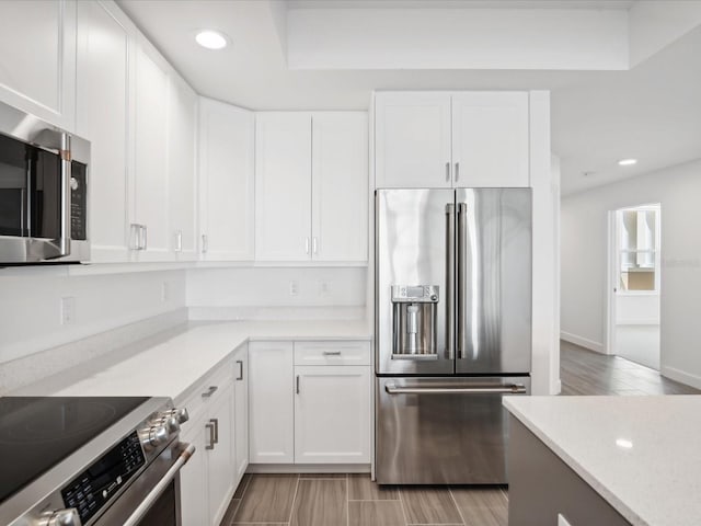 kitchen featuring premium appliances, light stone countertops, white cabinetry, a tray ceiling, and light hardwood / wood-style flooring