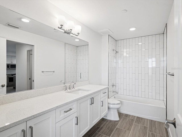 full bathroom with tiled shower / bath, toilet, tile floors, and vanity