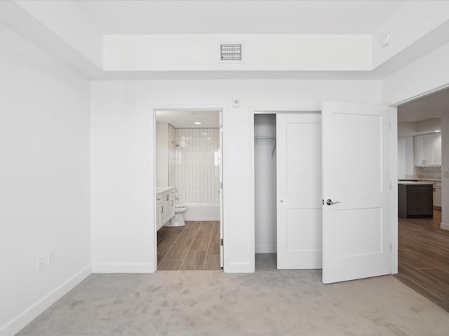 unfurnished bedroom featuring a closet, ensuite bath, and light colored carpet