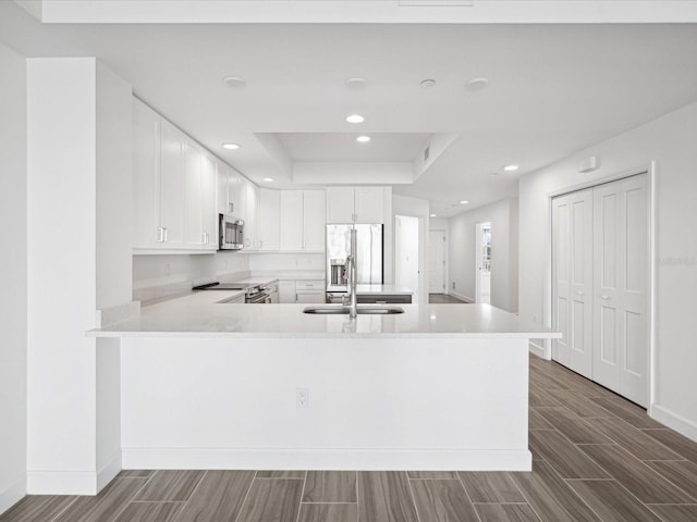 kitchen featuring kitchen peninsula, sink, white cabinets, stainless steel appliances, and a tray ceiling