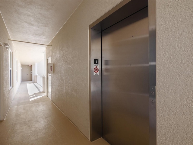 hall featuring a textured ceiling and elevator