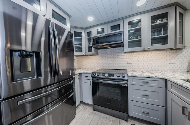 kitchen with stainless steel appliances, light hardwood / wood-style flooring, gray cabinetry, backsplash, and light stone counters