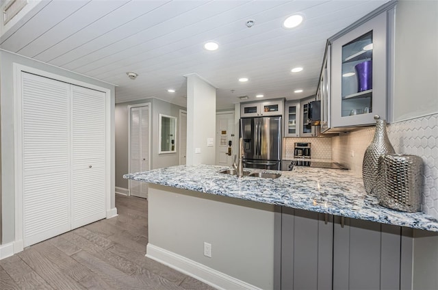 kitchen featuring kitchen peninsula, light stone counters, wood-type flooring, tasteful backsplash, and stainless steel refrigerator with ice dispenser