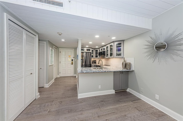 kitchen featuring dark wood-type flooring, stainless steel fridge, sink, light stone counters, and tasteful backsplash