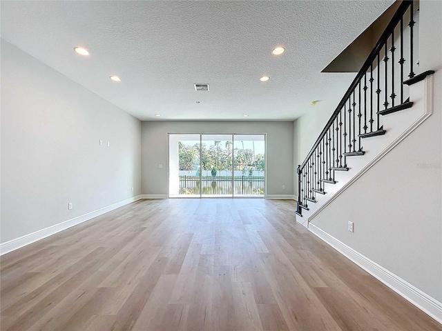 unfurnished living room featuring stairway, baseboards, a textured ceiling, and light wood finished floors